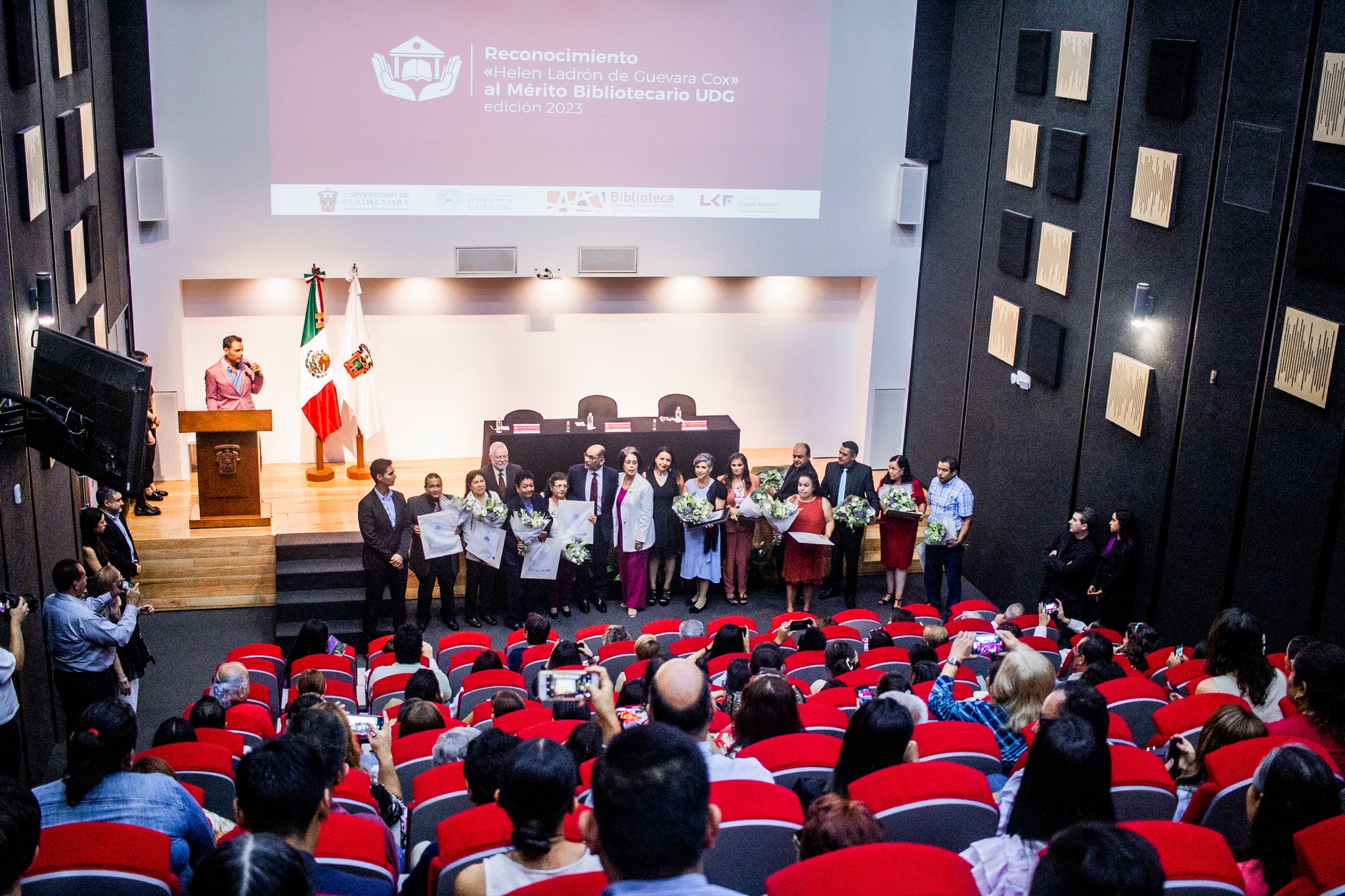 Bibliotecarios reconocidos junto a autoridades del evento en auditorio frente a asistentes