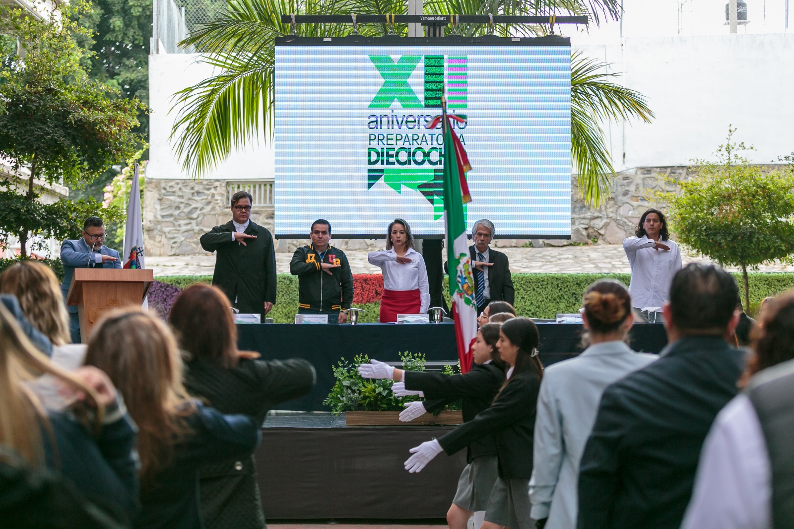 Autoridades del evento de pie en presidium frente a asistentes al evento sentados