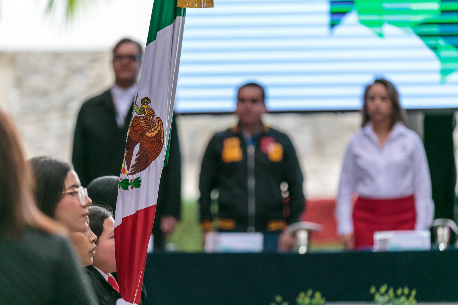 Autoridades del evento de pie en presidium frente a asistentes al evento sentados