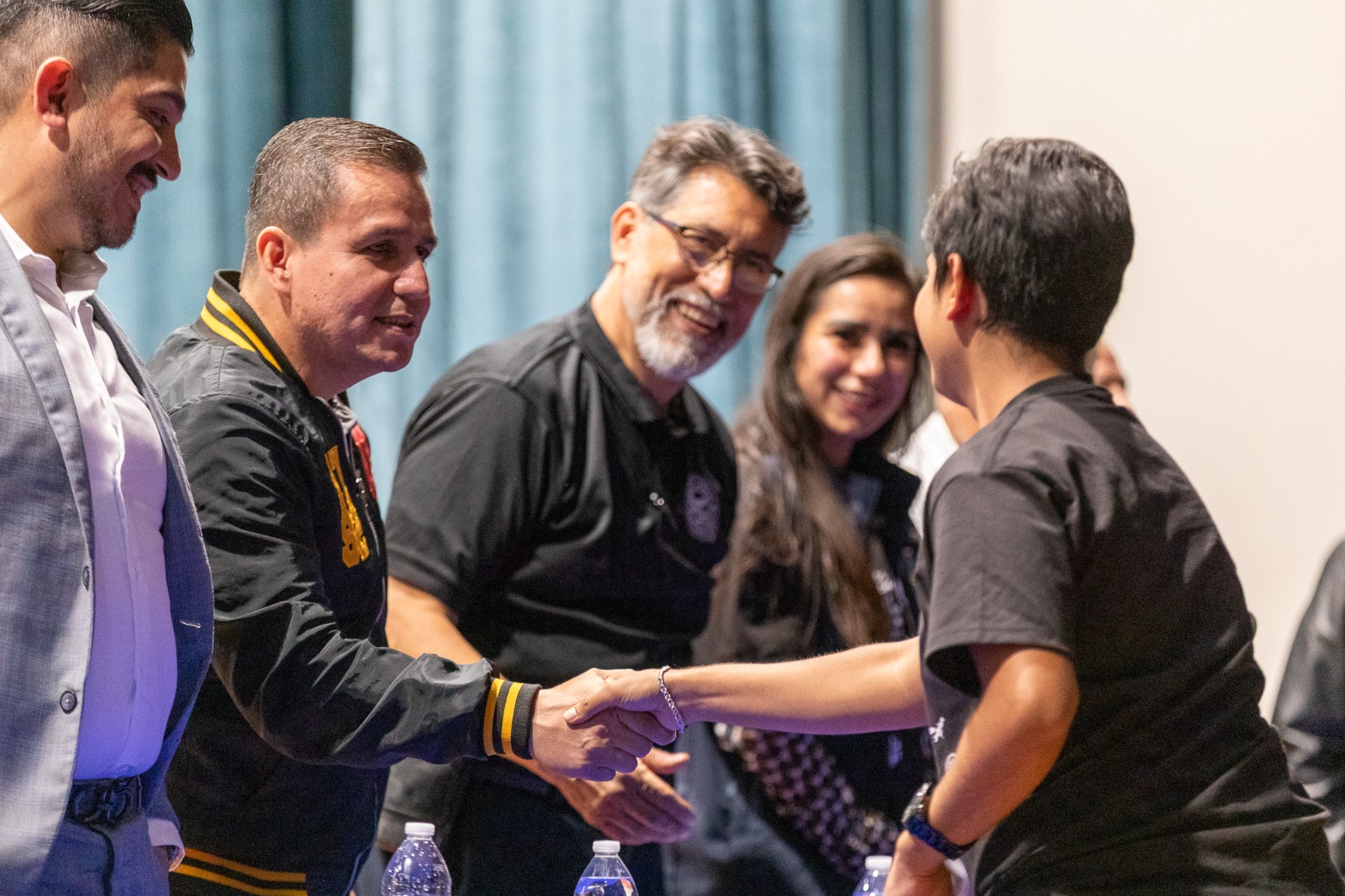 Autoridades del evento en presidium saludan de mano a jóven