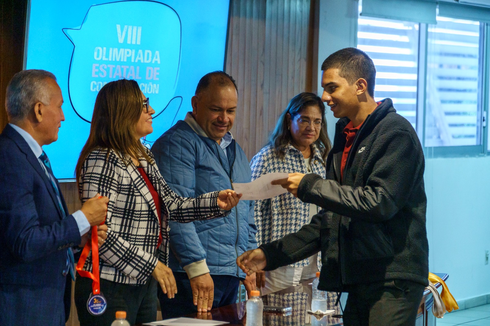 Autoridades del evento en presidium entregando diploma y medalla a alumno que gano concurso