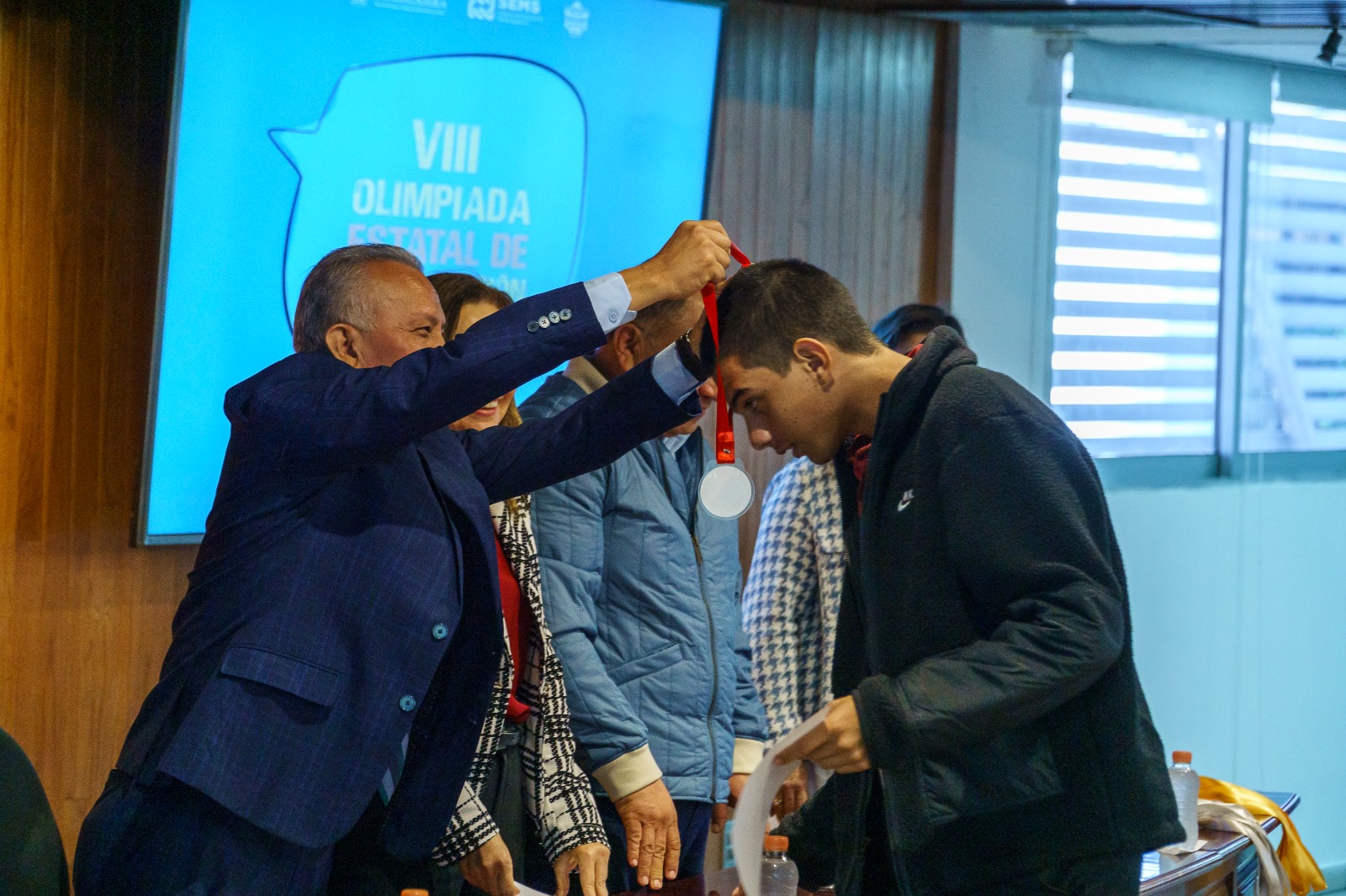 Autoridades del evento en presidium entregando diploma y medalla a alumno que gano concurso