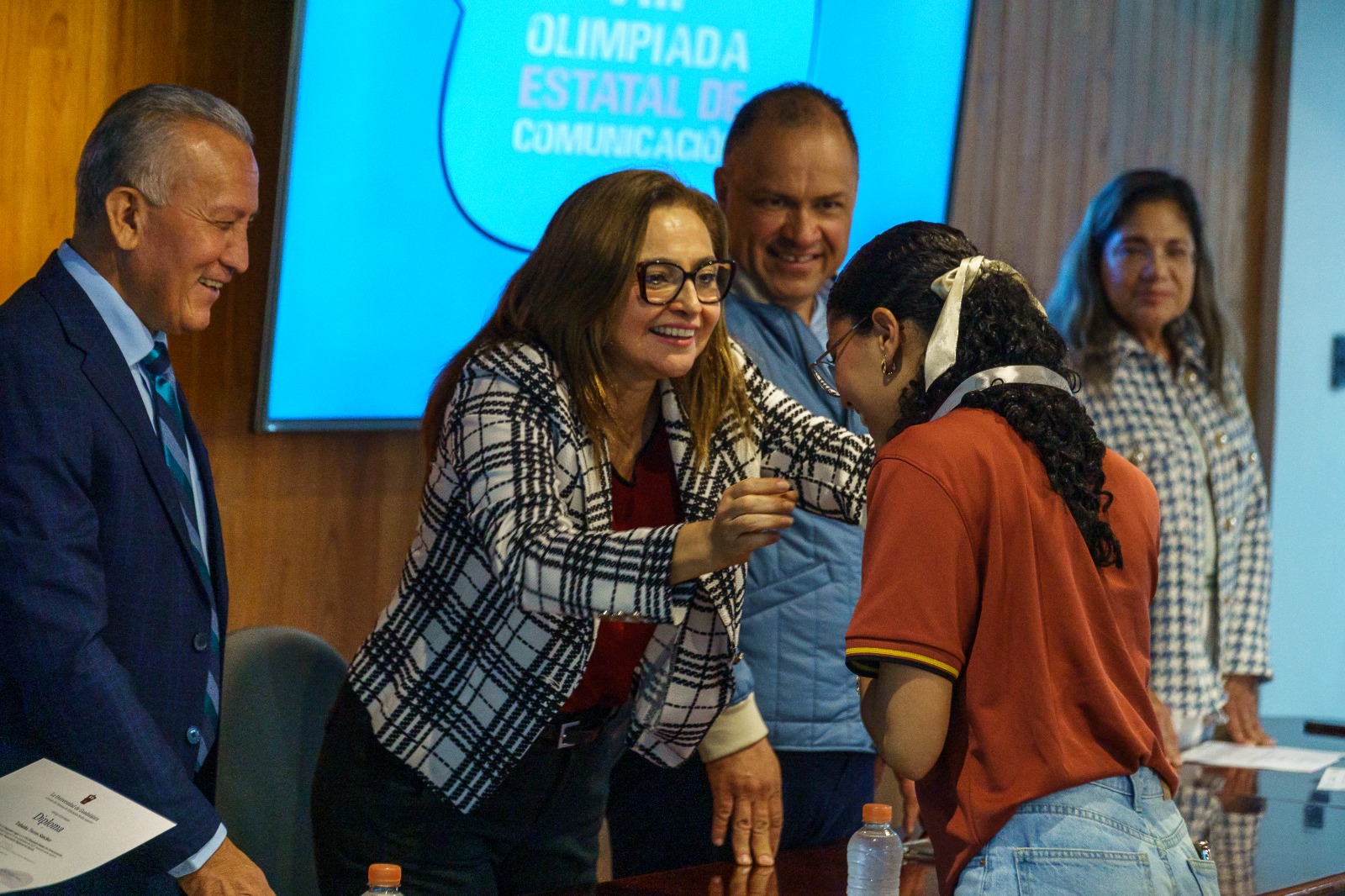 Autoridades del evento en presidium entregando diploma y medalla a alumna que gano concurso