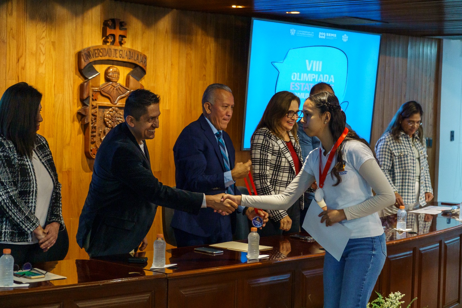 Autoridades del evento en presidium entregando diploma y medalla a alumna que gano concurso
