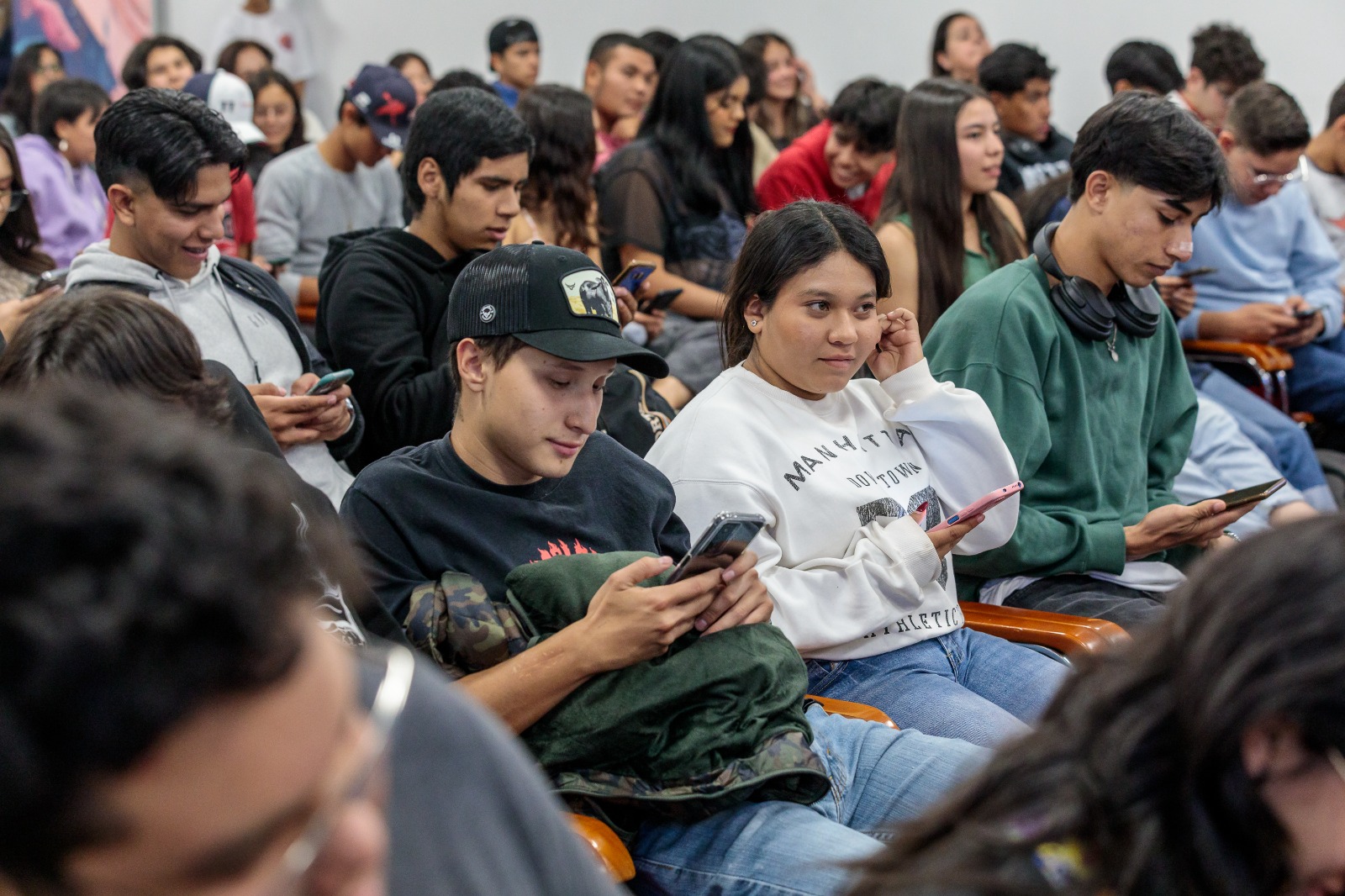 Asistentes al evento sentados usan su celular