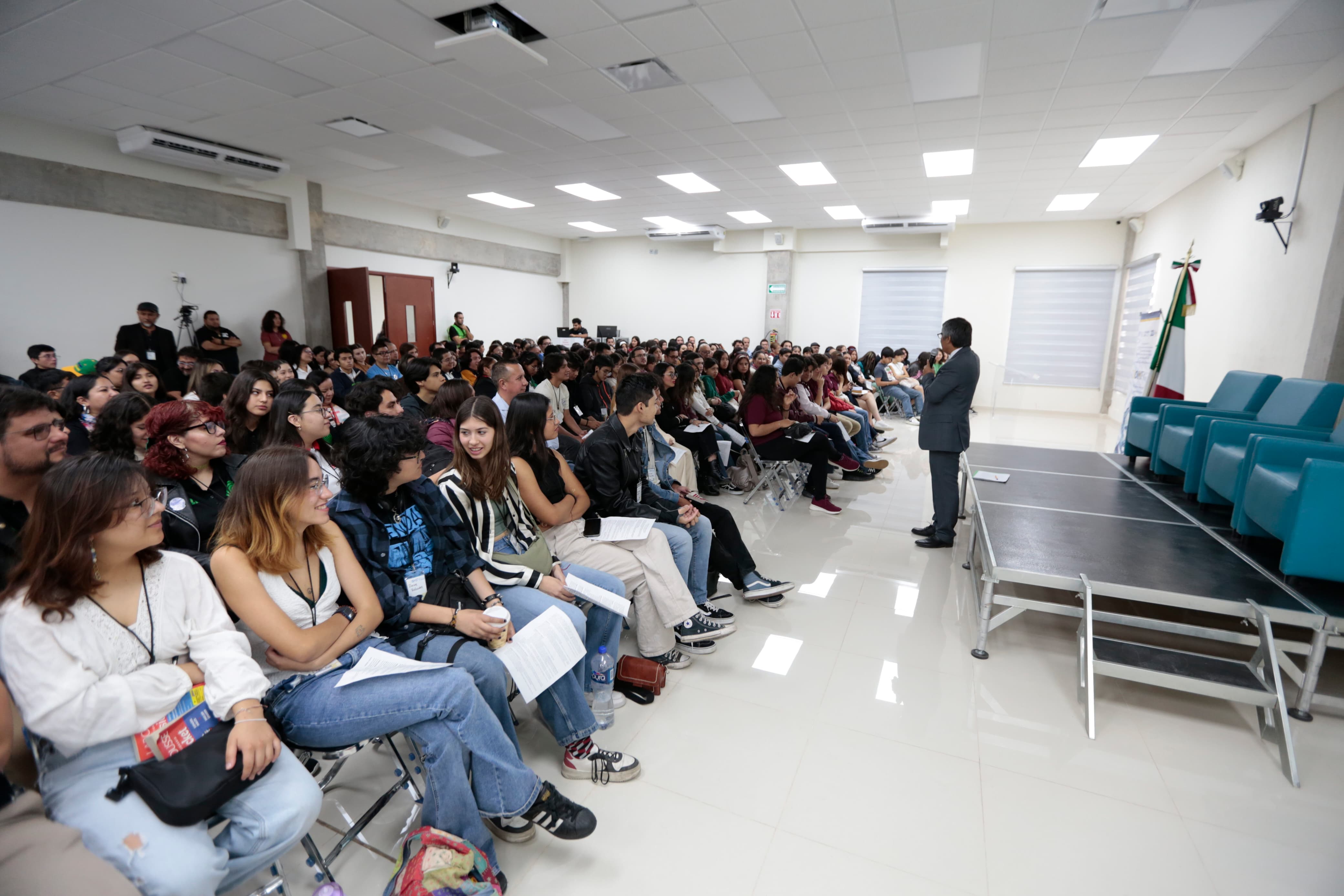 Autoridades del evento de pie en presidium frente a asistentes al evento sentados