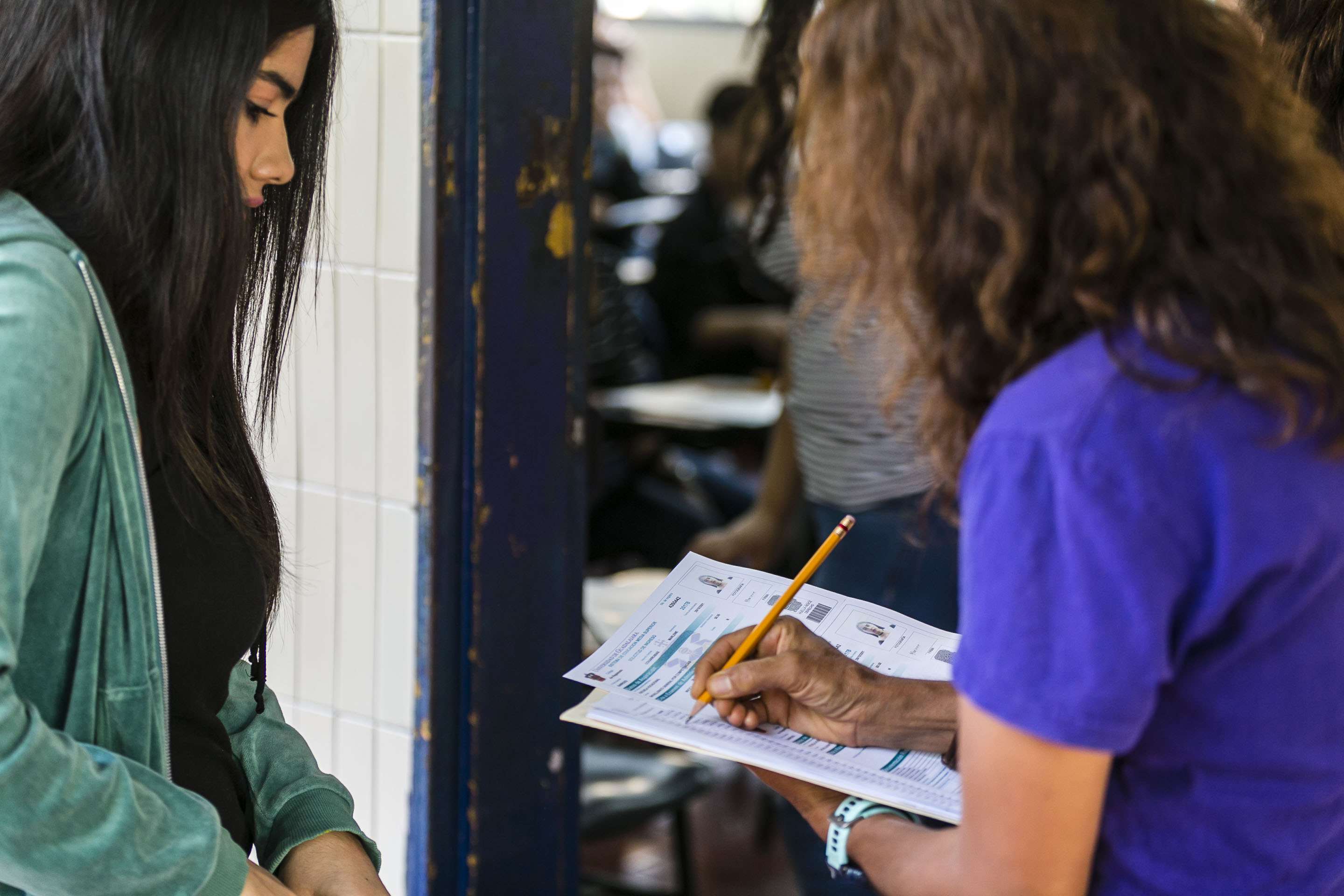 Instructor revisa cédula de aspirante al ingreso del aula para el examen Piense II