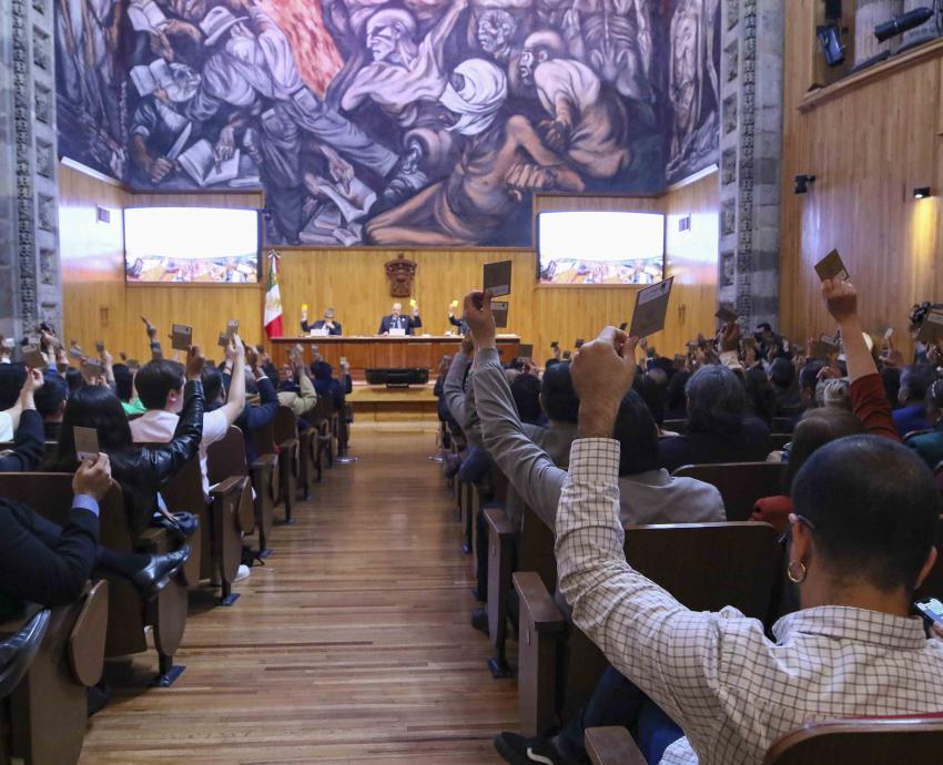 consejeros universitarios sentados en auditorio emitiendo su voto