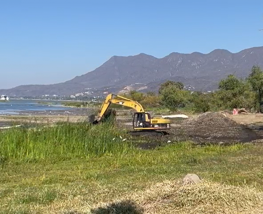 retroexcavadora amarilla con brazo de pistón hidráulico realiza trabajos en un costado de lago