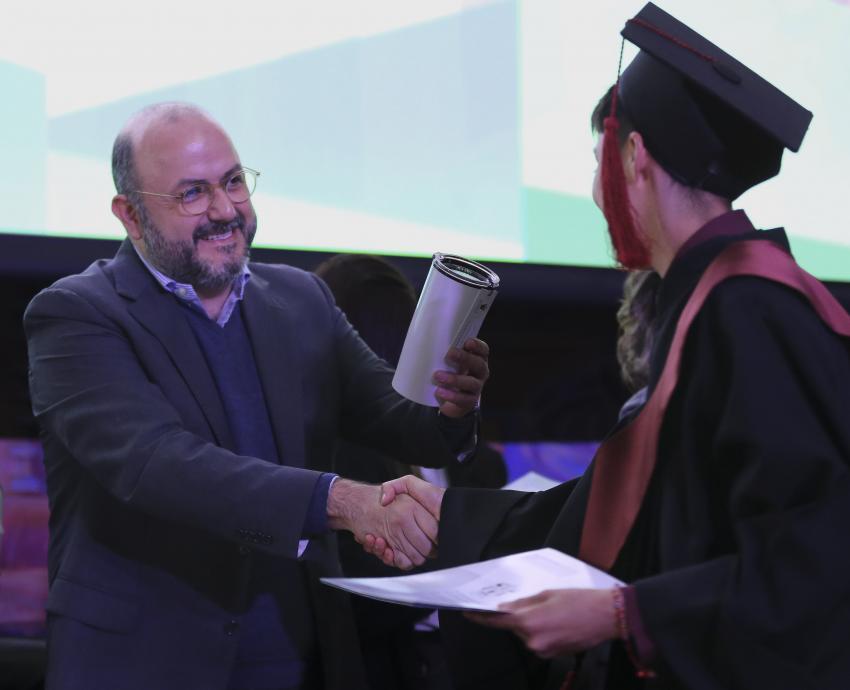 rector general de la Universidad de Guadalajara doctor Ricardo Villanueva Lomelí entregando presente a graduado