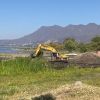 retroexcavadora amarilla con brazo de pistón hidráulico realiza trabajos en un costado de lago